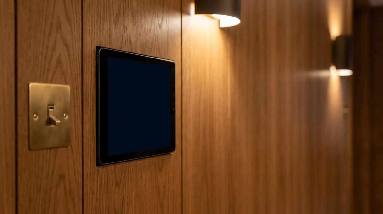 A slim control tablet set into a warm oak-paneled wall